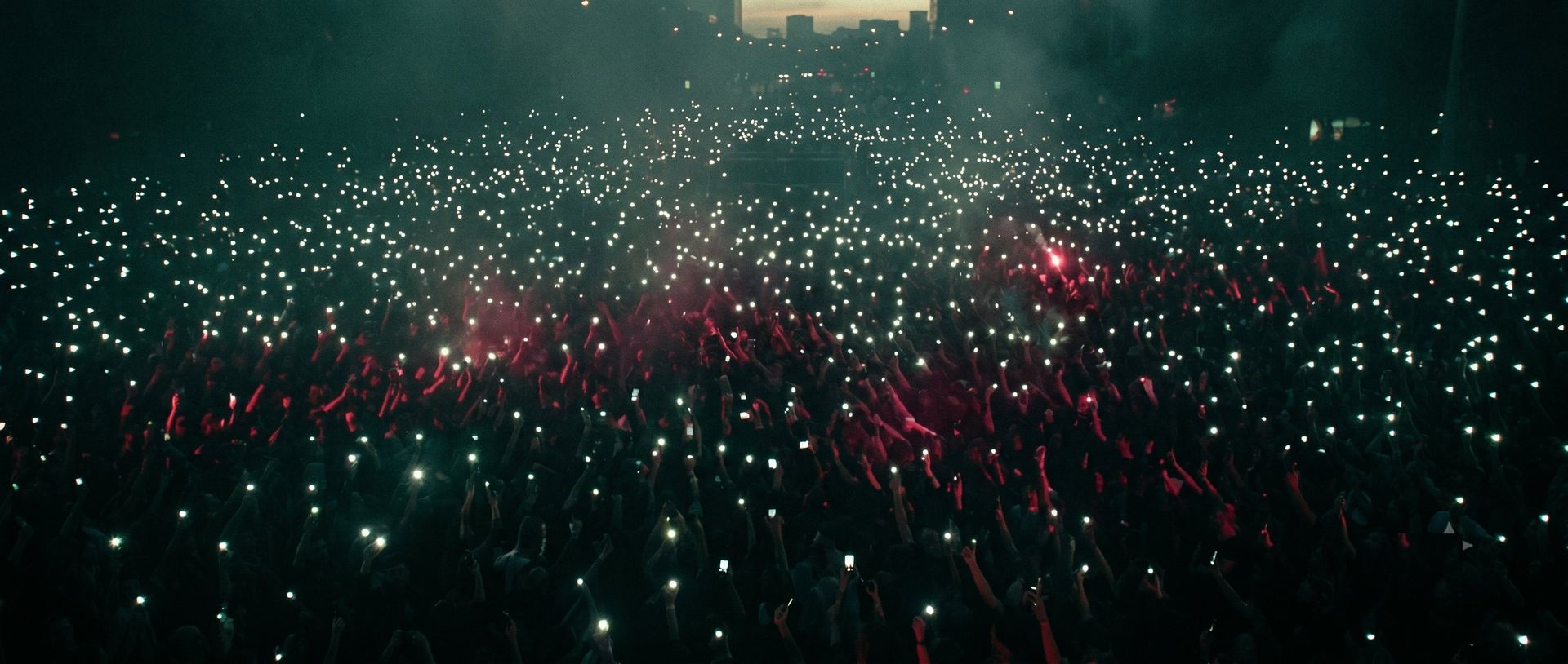 A vast crowd at dusk holding up phone lights