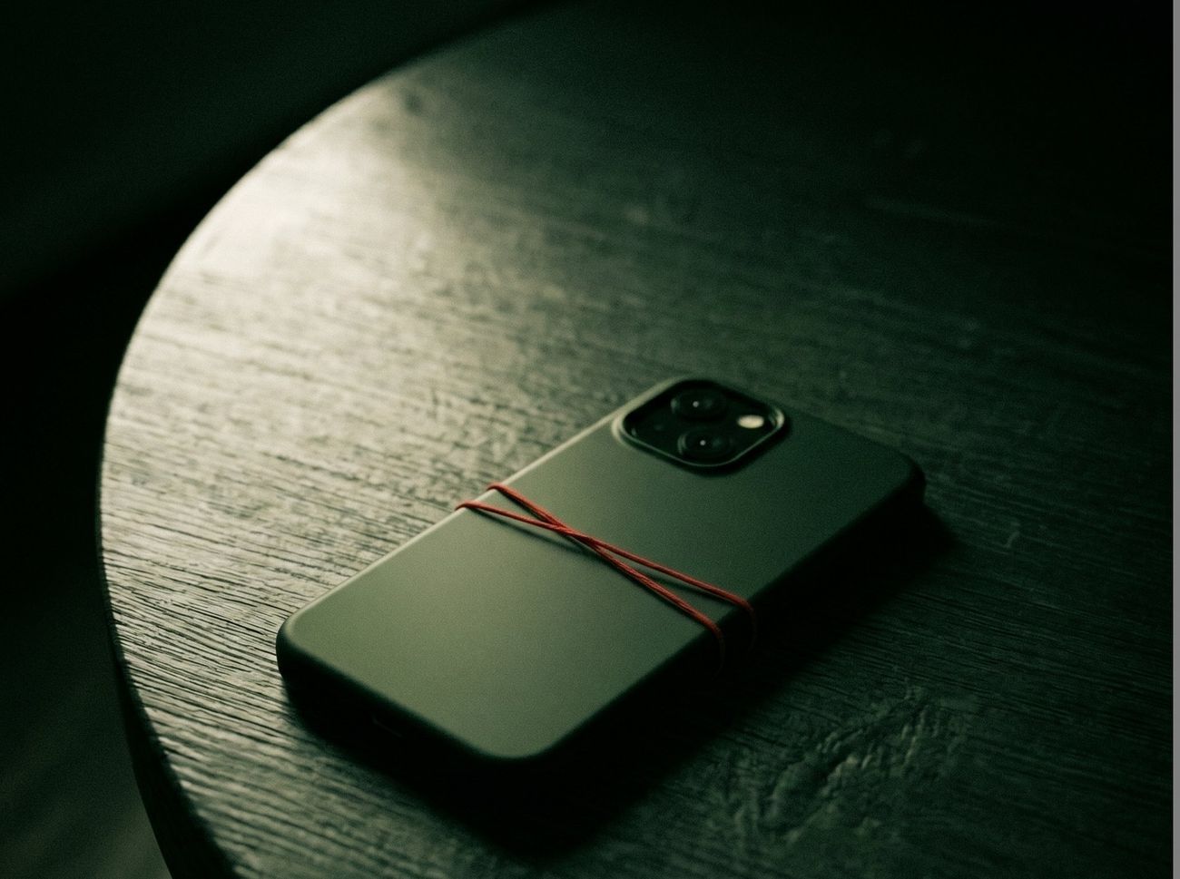 A phone lying face down on a wooden table, tied with a red thread